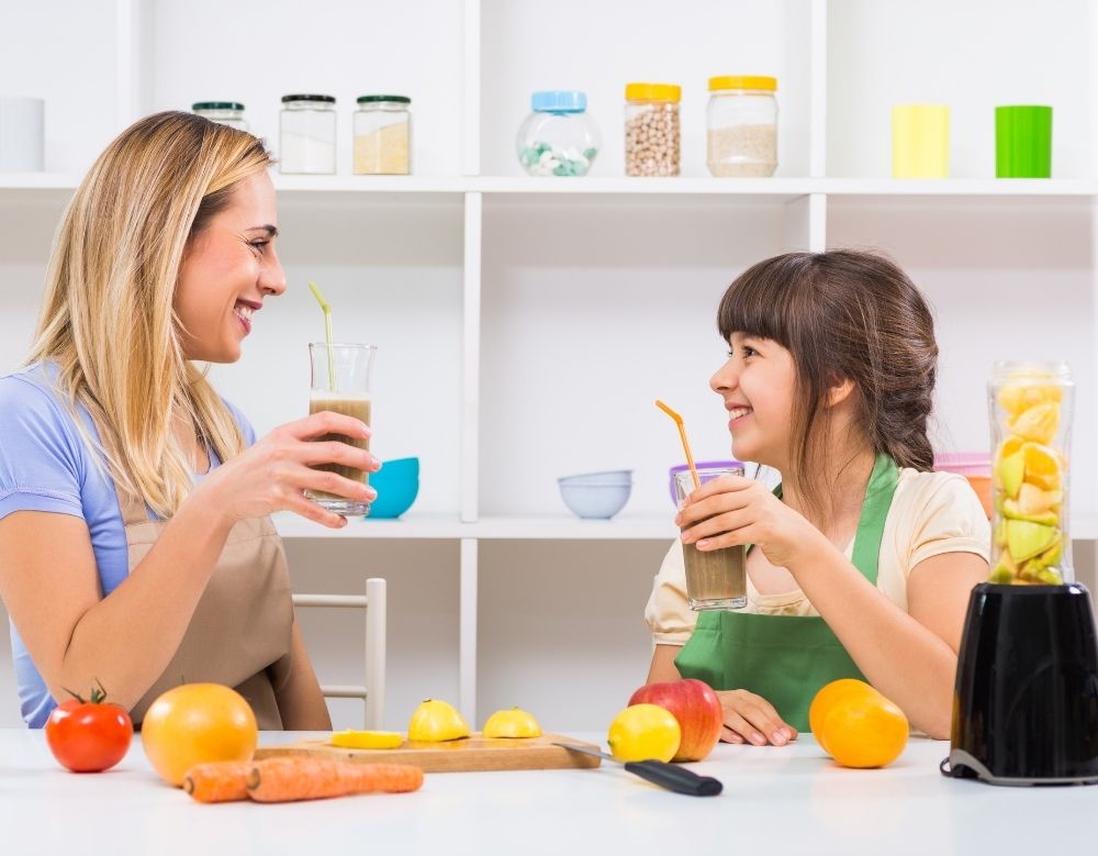 A parent and child laughing while making a healthy fruit smoothie